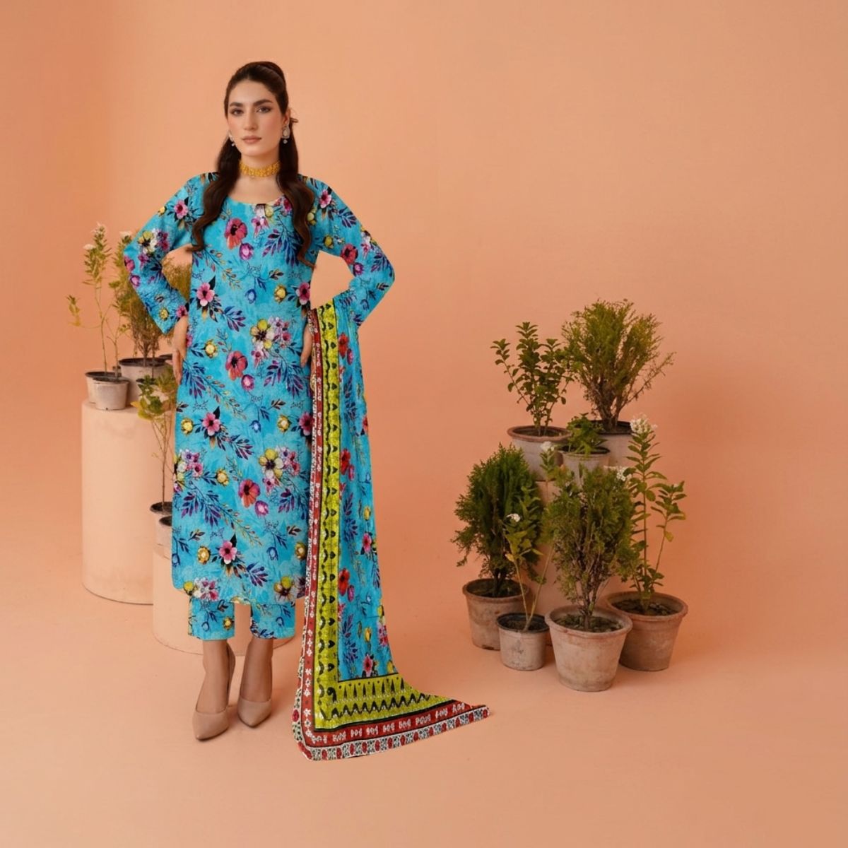 Woman in a blue floral dress standing next to potted plants on a peach background