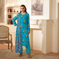 Woman in a blue floral traditional outfit standing in a room with a fireplace and chair.